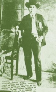 Amelio Robles Ávila in suit, tie, boots, and hat with hand on holstered gun at hip