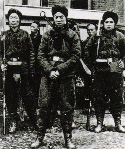 Three male Boxer soldiers wearing turbans and holding weapons, two other soldiers in background