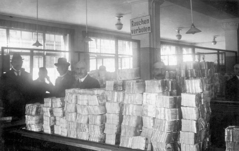 Tall piles of money on table waiting to be distributed with men standing behind the large stacks of money