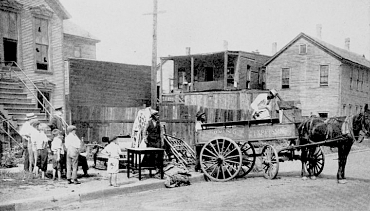A Black family loading their positions onto a horse-drawn carriage as they leave their damaged home after the 1919 Chicago race riot while a group of small children watch