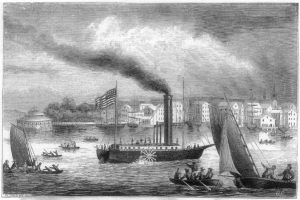 Ship with stack in middle blowing smoke and American flag on stern, floating on water surrounded by other ships, town in the background