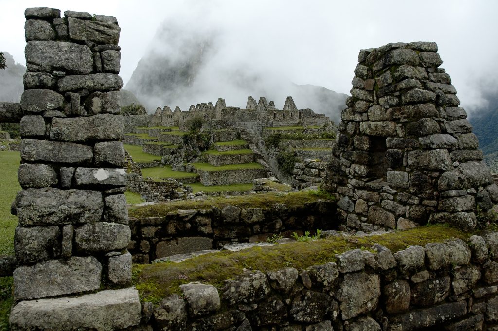 Buildings made of stone blocks missing roofs with large mountain covered by mist in the background