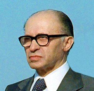 Colored photograph of Menachem Begin with dark rimmed glasses and suit and tie