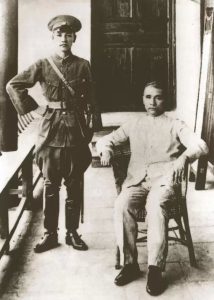 Sun Yat-sen in light colored suit seated in a chair with Chiang Kai-shek in military dress standing next to him