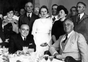 Getúlio Vargas (left) and Franklin Delano Roosevelt (right) sitting a table with a group of people behind them