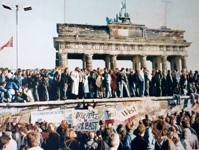 Large group of Germans standing on top of the Berlin Wall in front of the Brandenburg Gate many holding up signs