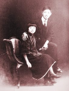 Wedding photo of two young Chinese revolutions sitting in chair and smiling at camera