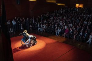 person in wheelchair on a stage in front of an audience
