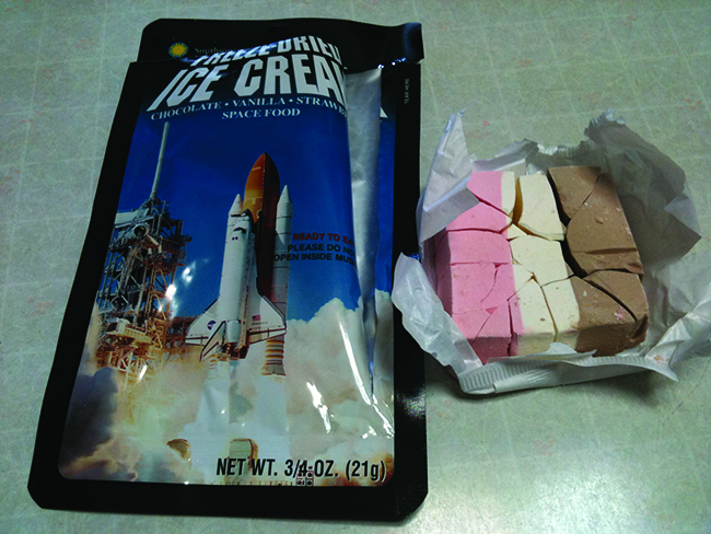 A photograph shows a package with a rocket being launched on the front and a block of pink, white and brown striped solid in a wrapper next to it.