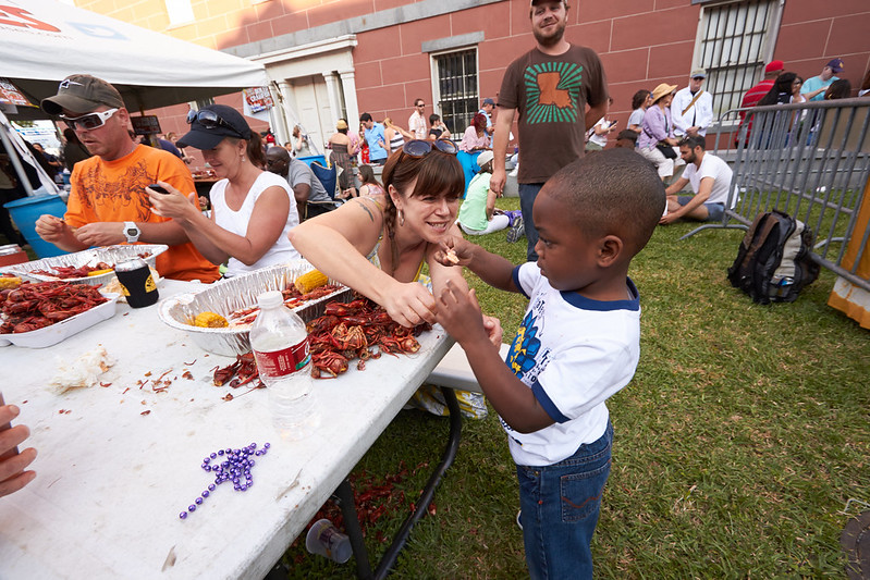 Young boy in the foreground is holding a crawfish tail while a woman leans over and is smiling.