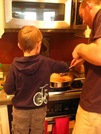 A boy helping his father cook at a stove