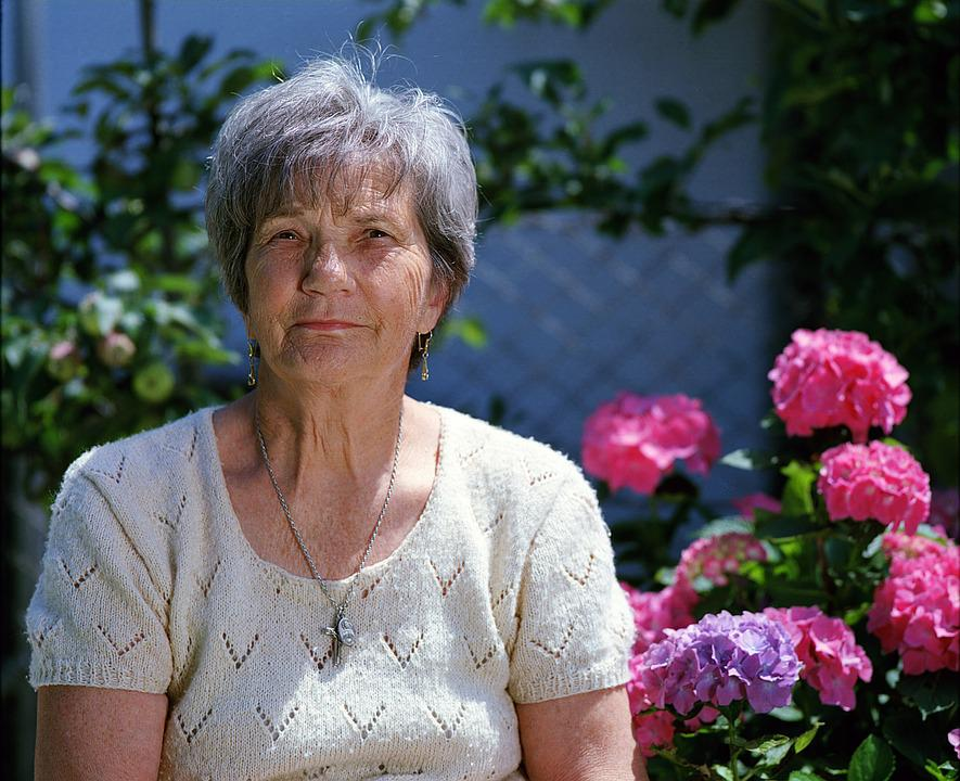 An older woman sitting next to purple and pink flowers