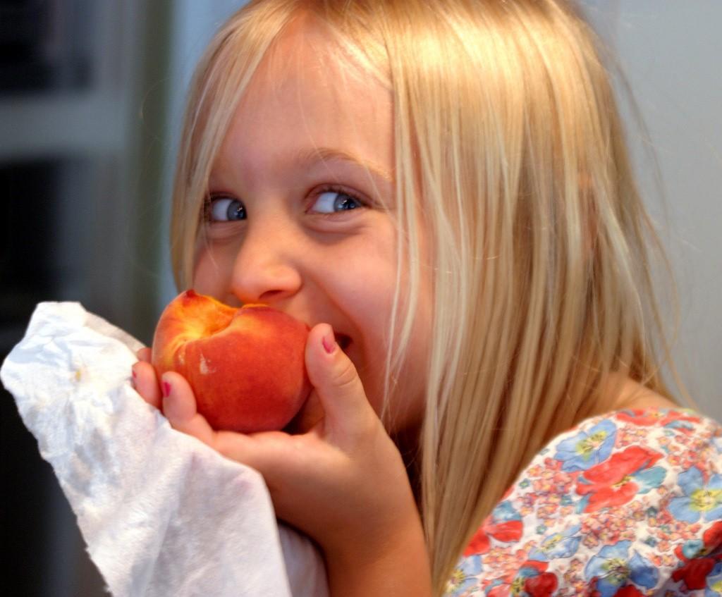 A little girl eating a peach
