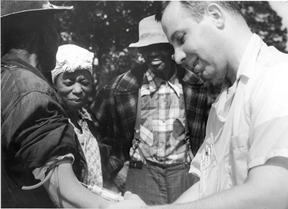 A white man injecting a black man with a syringe while a black woman and black man watch.