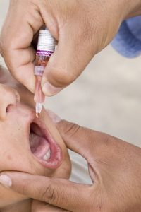 Photo shows a child receiving an oral vaccination from a dropper.
