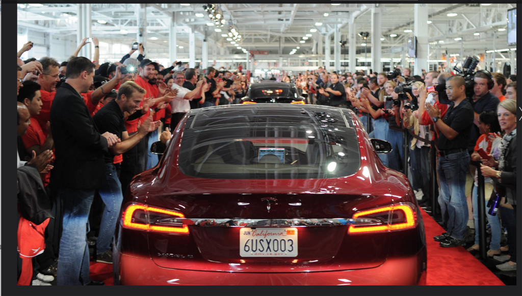 Large crowd gathered around a red Tesla.