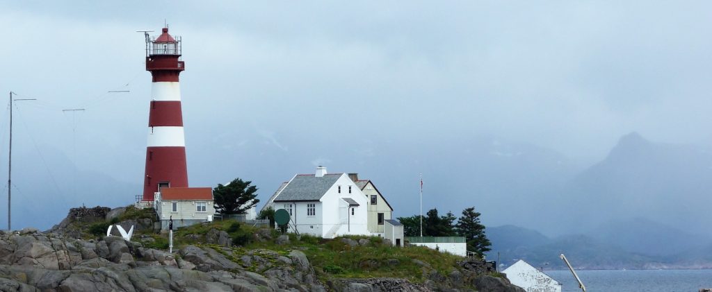 A photograph shows a lighthouse sitting on a bluff near the ocean.