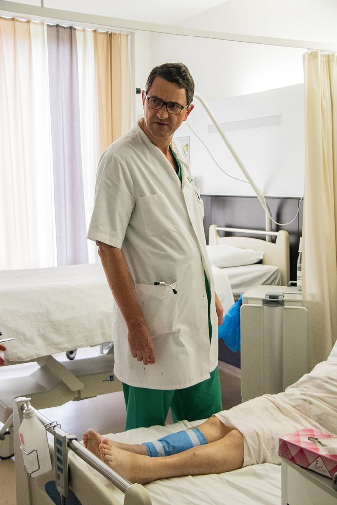 A photograph shows a doctor in a recover room, standing beside a patient.