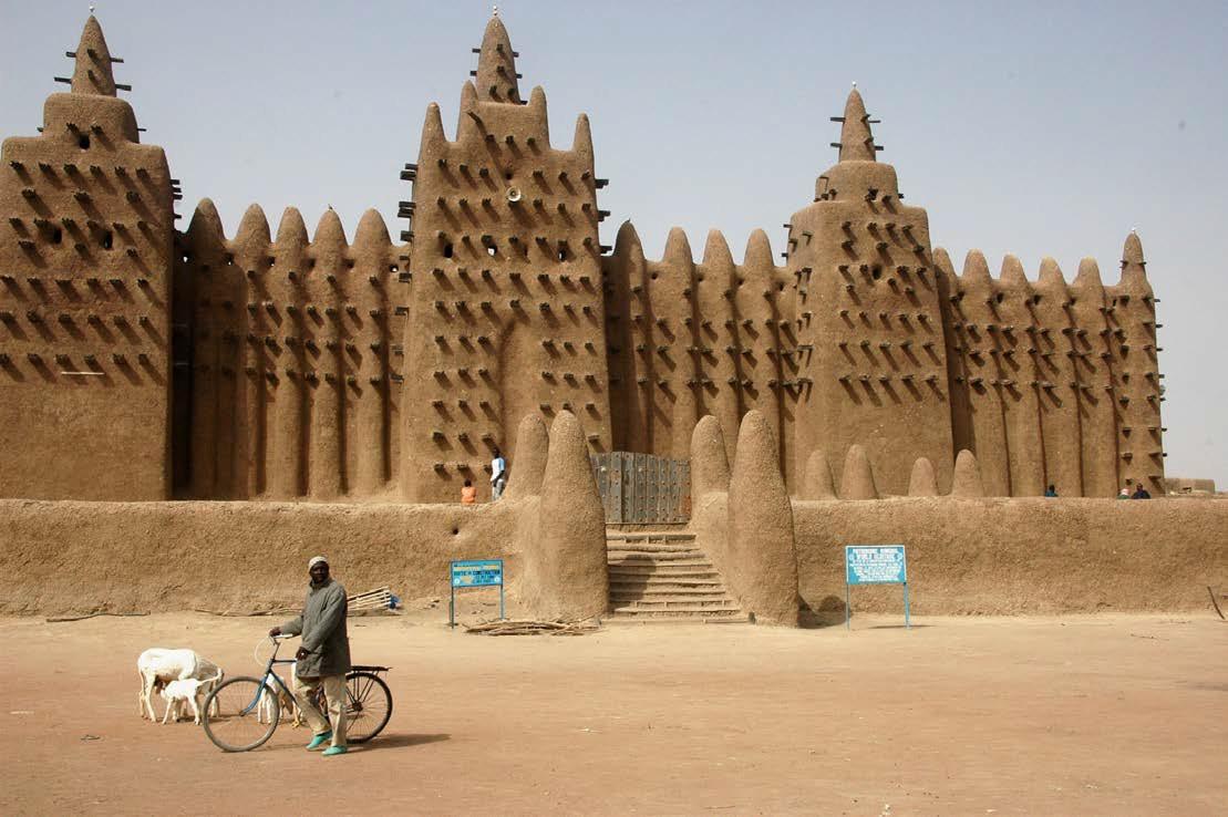 The Great Mosque in Djenne with a man by a bike and two dogs in front of the Mosque.