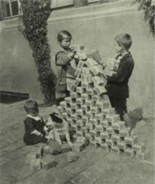 Three children play with stacks of banknotes. Two of the children use them to build a pyramid almost as tall as themselves. The third child sits with a dog nearby among a pile of banknotes.