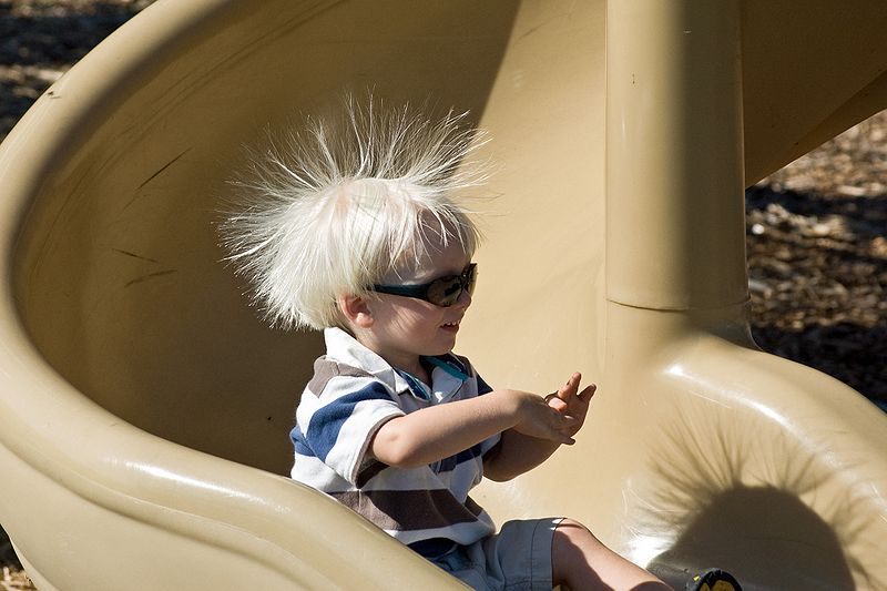 A child swoops down a plastic playground slide, his hair standing on end.