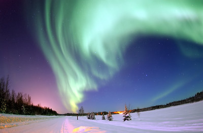 A shimmering curtain of green lights in the sky above a snow covered landscape. Stars are visible in the dusky sky beyond the lights.