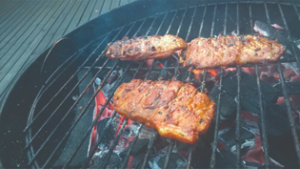 A photograph of meat being cooked on a charcoal grill.