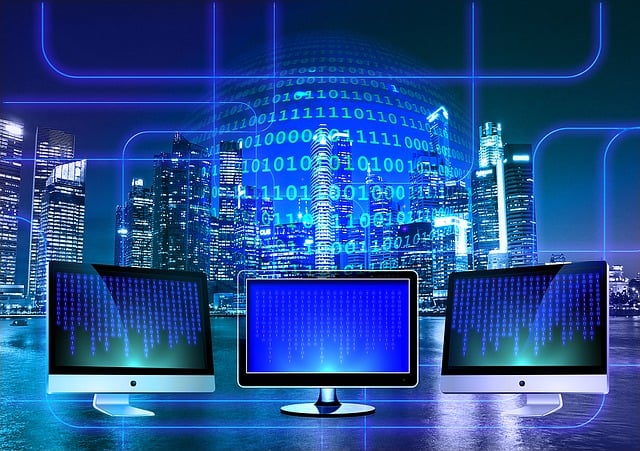 A photo of three computer monitors in front of a window with a city skyline in the background. There is binary coding reflecting in the window.