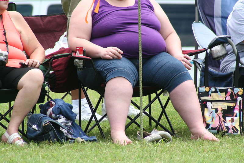 Photo of an obese woman sitting at an outdoor event and smoking a cigarette.