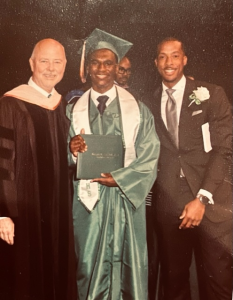 A high school graduate poses with faculty at graduation ceremony.