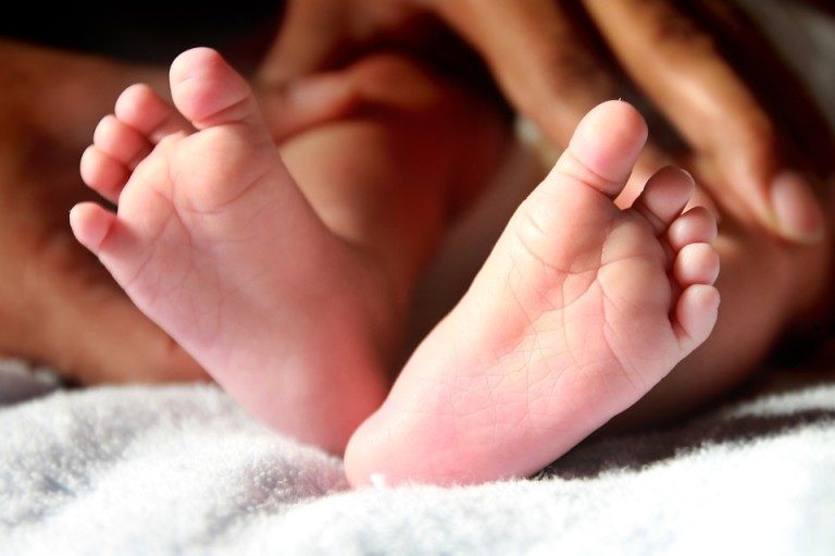 Photo of a newborn baby's feet and mother's hands in the background.