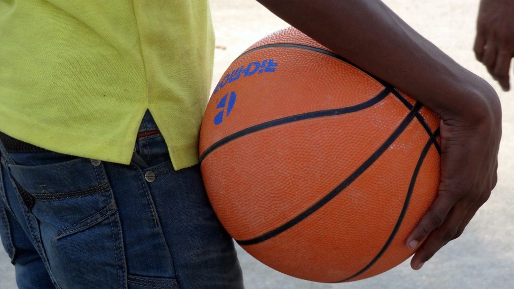 Child holding basketball between hand and body.