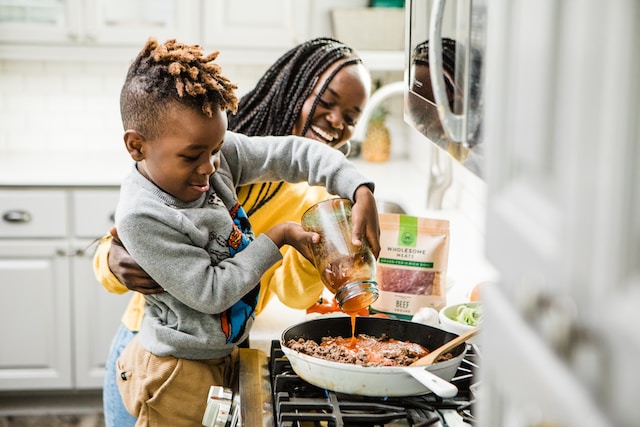 Photo shows a smiling mother and her son cooking dinner.