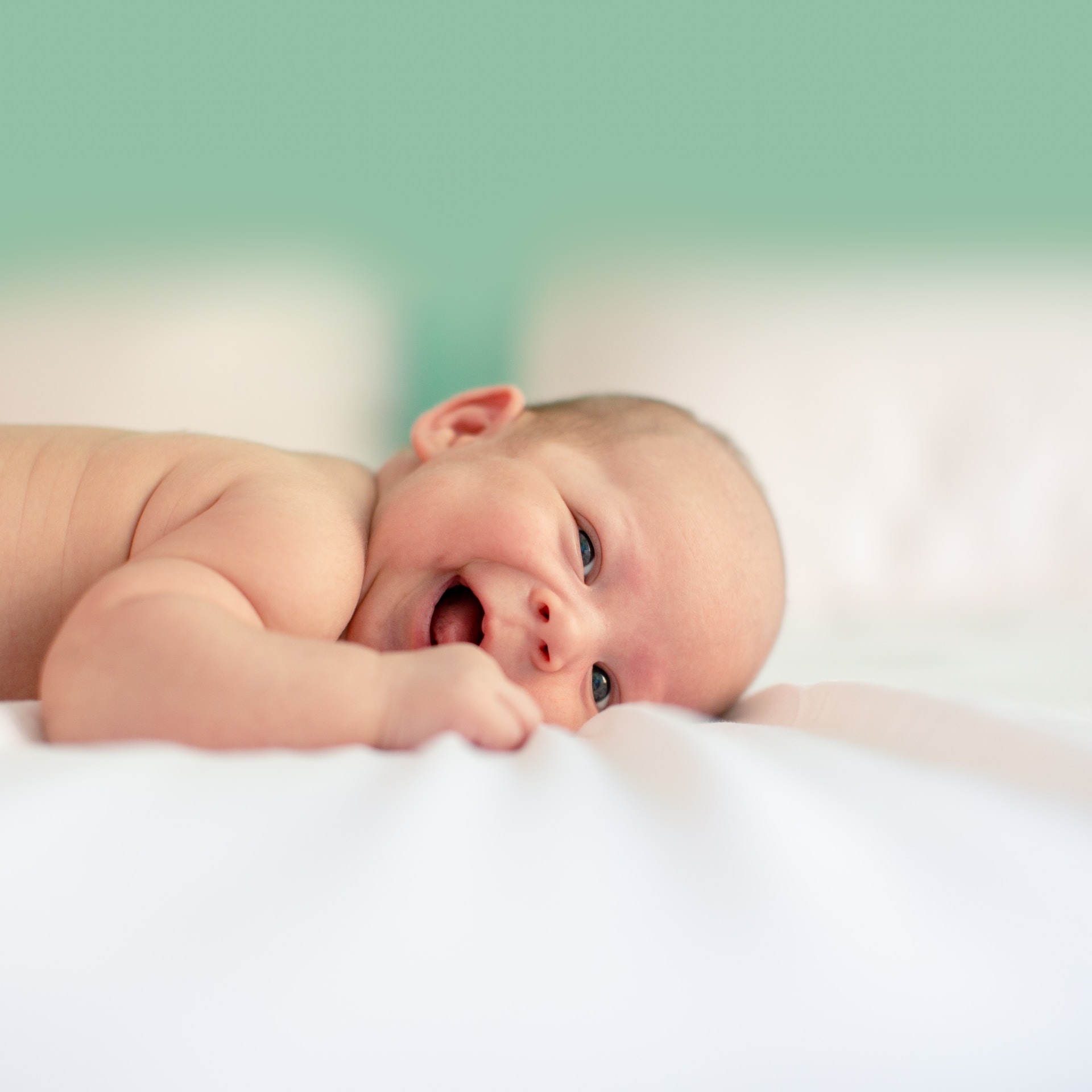 Photo of a smiling infant lying on a bed.