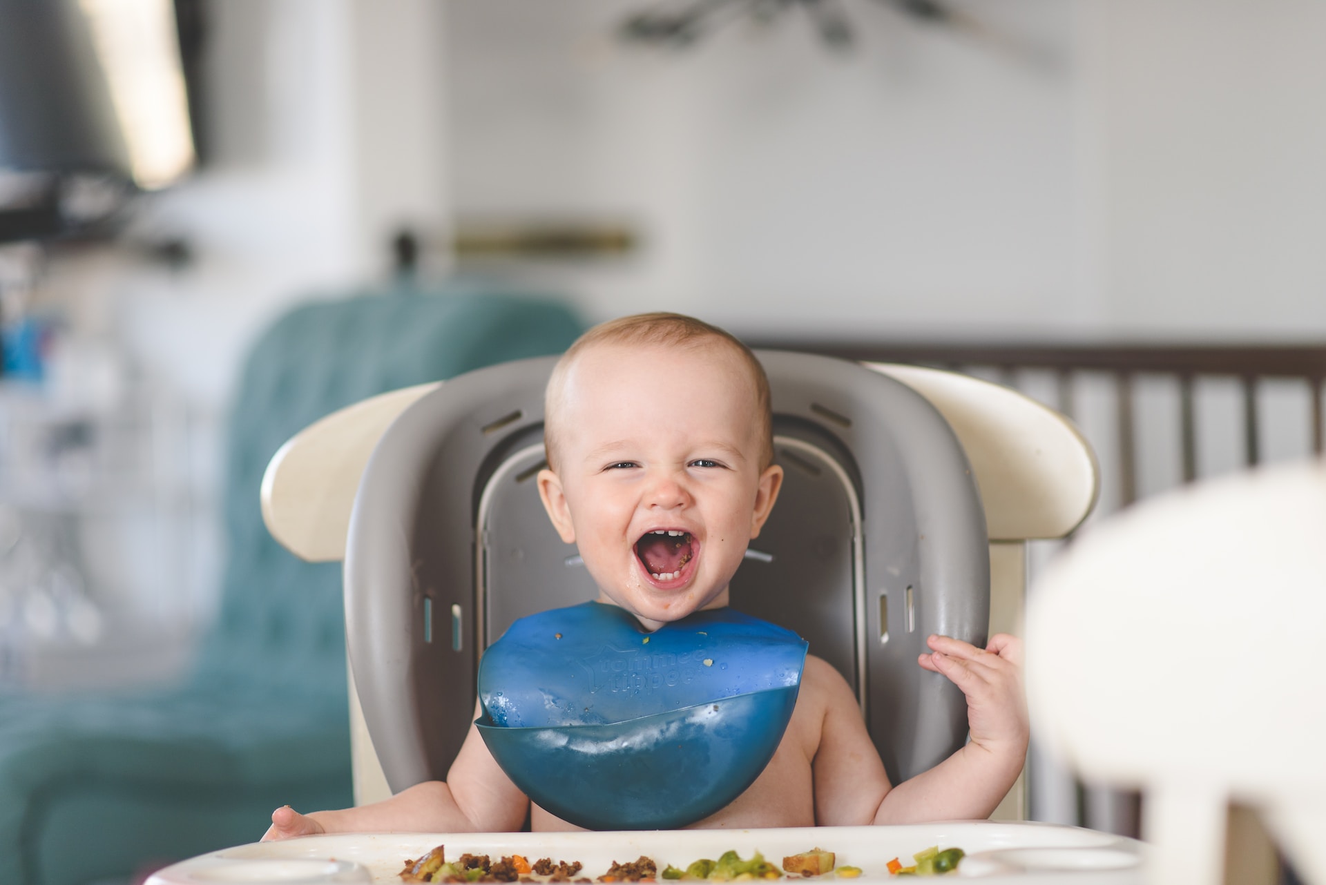 Photos shows a toddler sitting in a booster seat and eating vegetables.