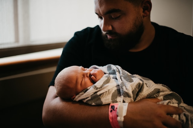 Photo shows a young father in a hospital holding his new baby.