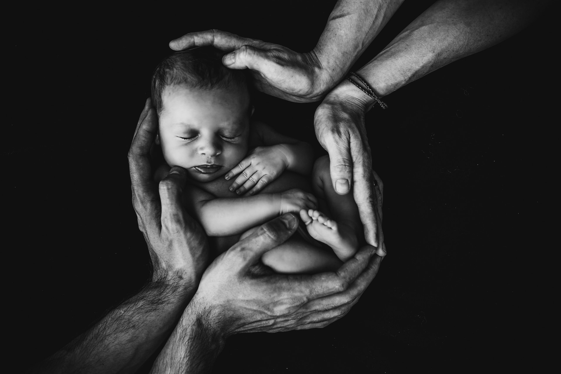 Photo shows a newborn baby surrounded by the hands of mother and father.