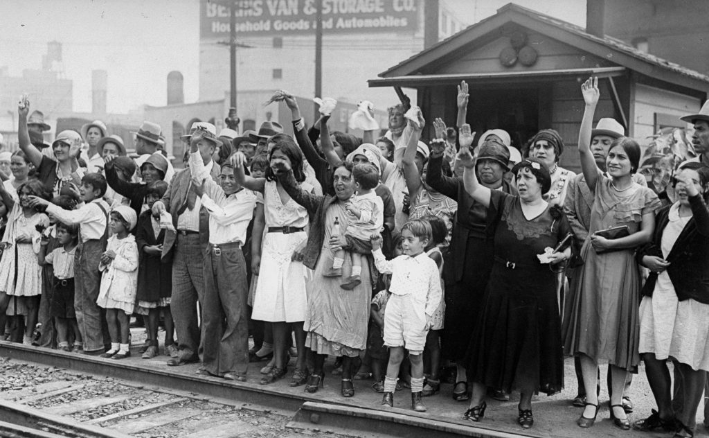 Black and white photograph of people waving goodbye at a train station.