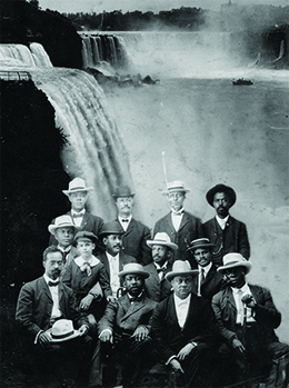 A photograph shows ten posed men, one of whom sits with a little boy. W. E. B. Du Bois is seated in the center.